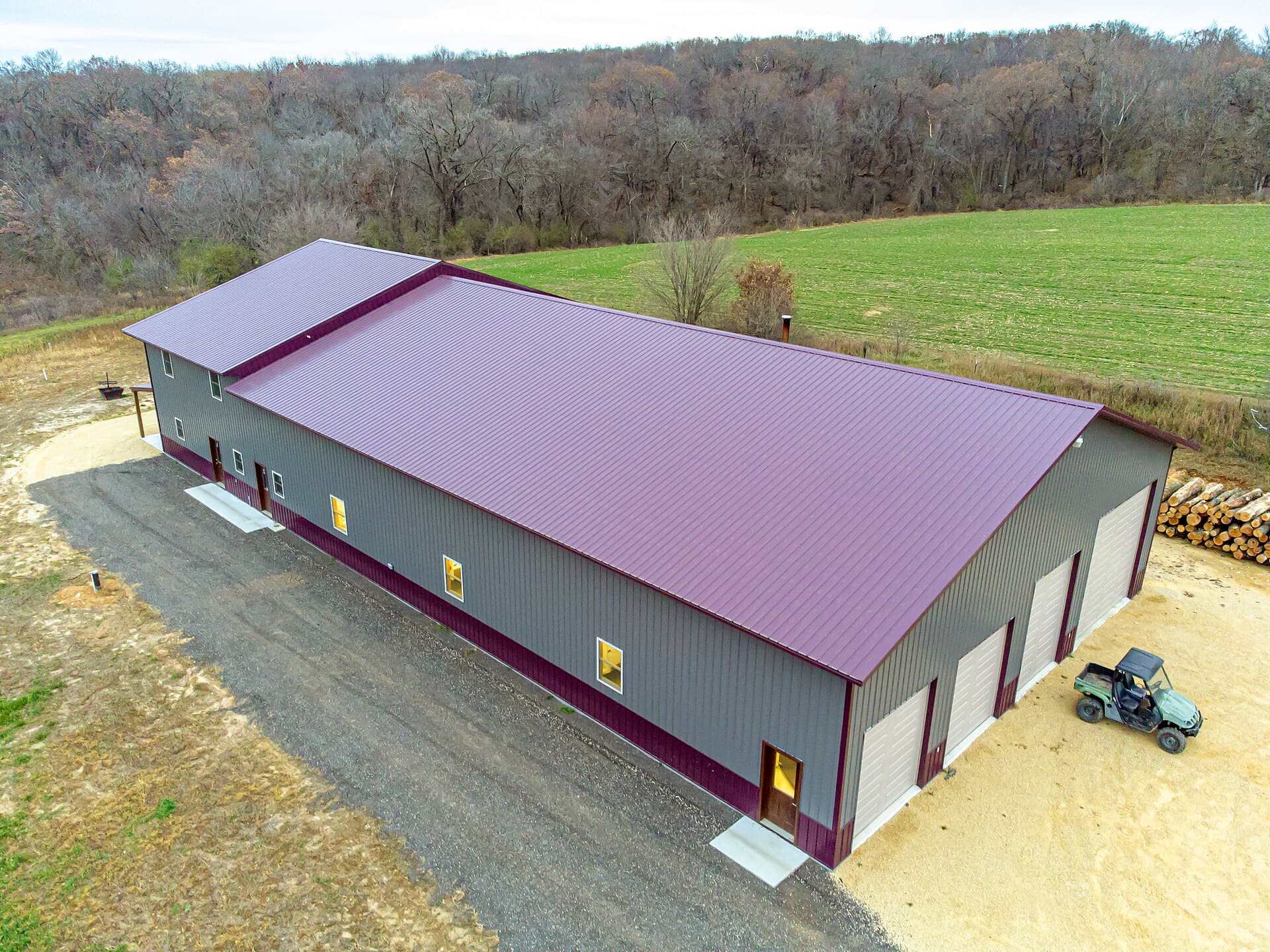 Finished post-frame pole barn with grey steel siding, red trim and overhead doors on a rural property